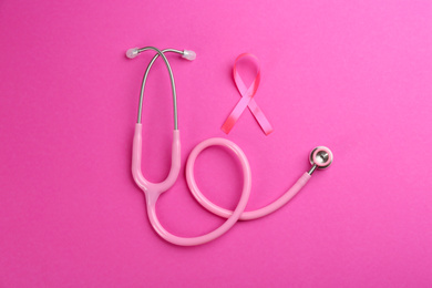 Photo of Pink ribbon as breast cancer awareness symbol and stethoscope on color background, flat lay