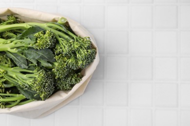 Photo of Bag with fresh raw broccolini on white tiled table, above view and space for text. Healthy food