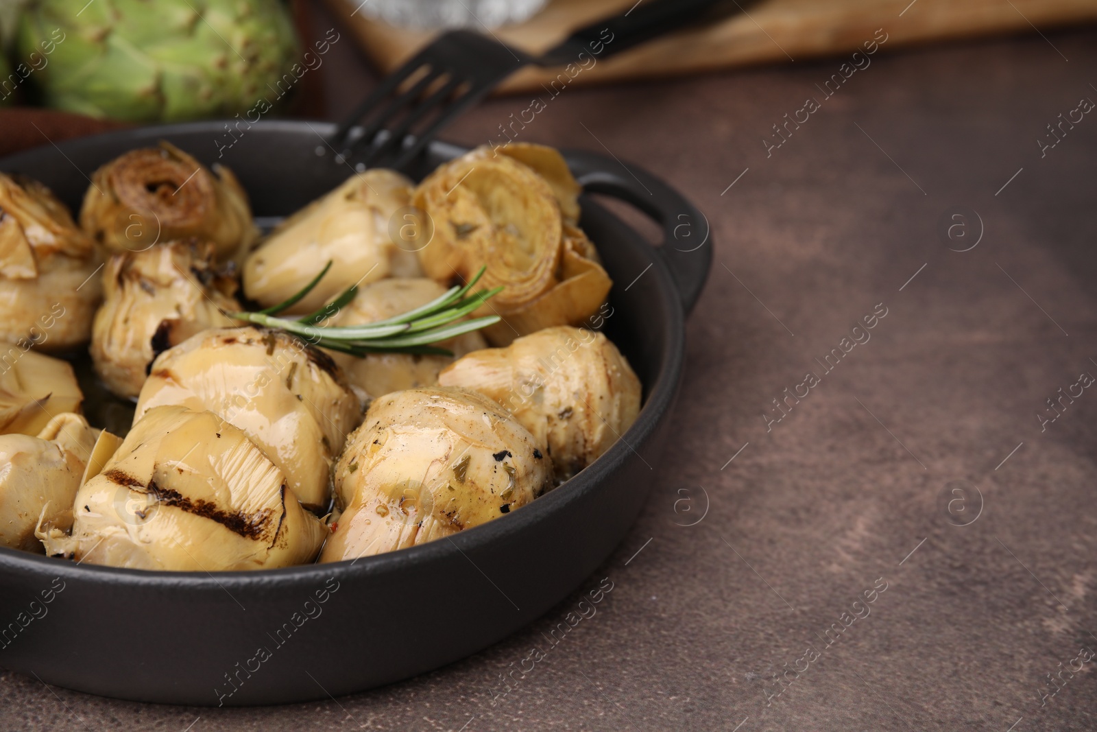 Photo of Delicious pickled artichokes with rosemary served on brown table, closeup. Space for text