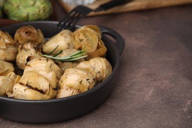 Photo of Delicious pickled artichokes with rosemary served on brown table, closeup. Space for text