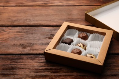 Photo of Partially empty box of chocolate candies on wooden table. Space for text
