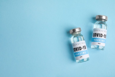 Photo of Vials with coronavirus vaccine on light blue background, flat lay. Space for text