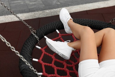 Photo of Woman in stylish sneakers sitting on swing outdoors, closeup