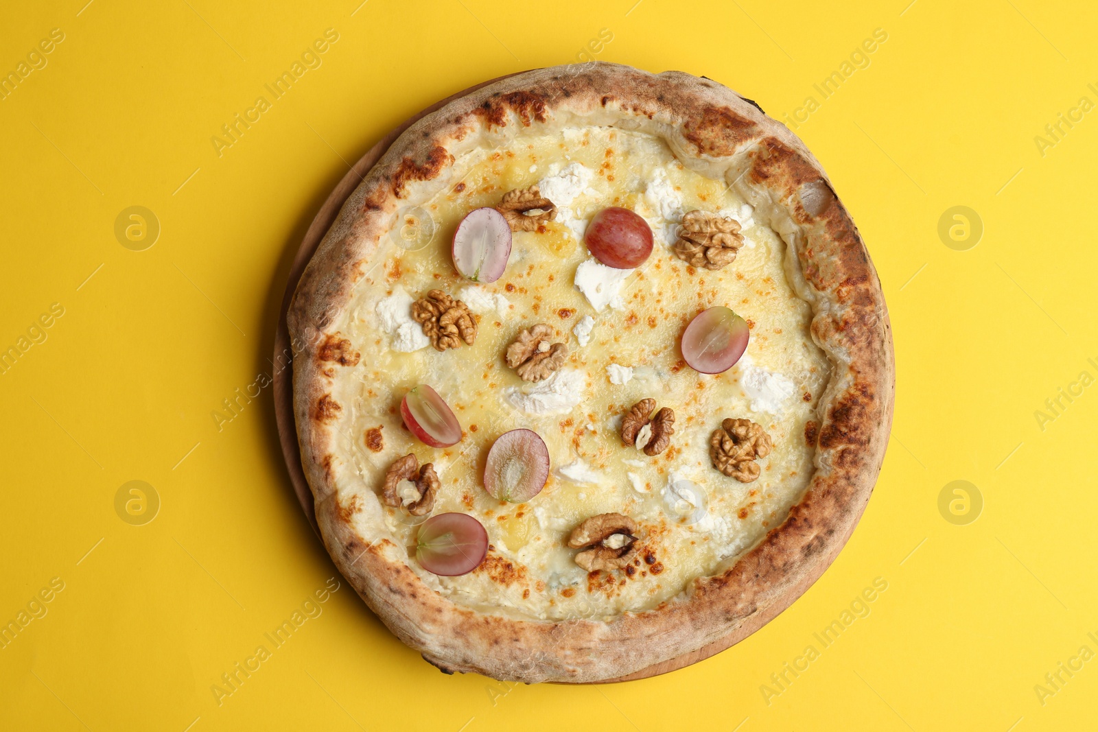 Photo of Delicious cheese pizza with grapes and walnuts on yellow background, top view