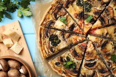 Photo of Delicious quiche with mushrooms and ingredients on light blue wooden table, flat lay