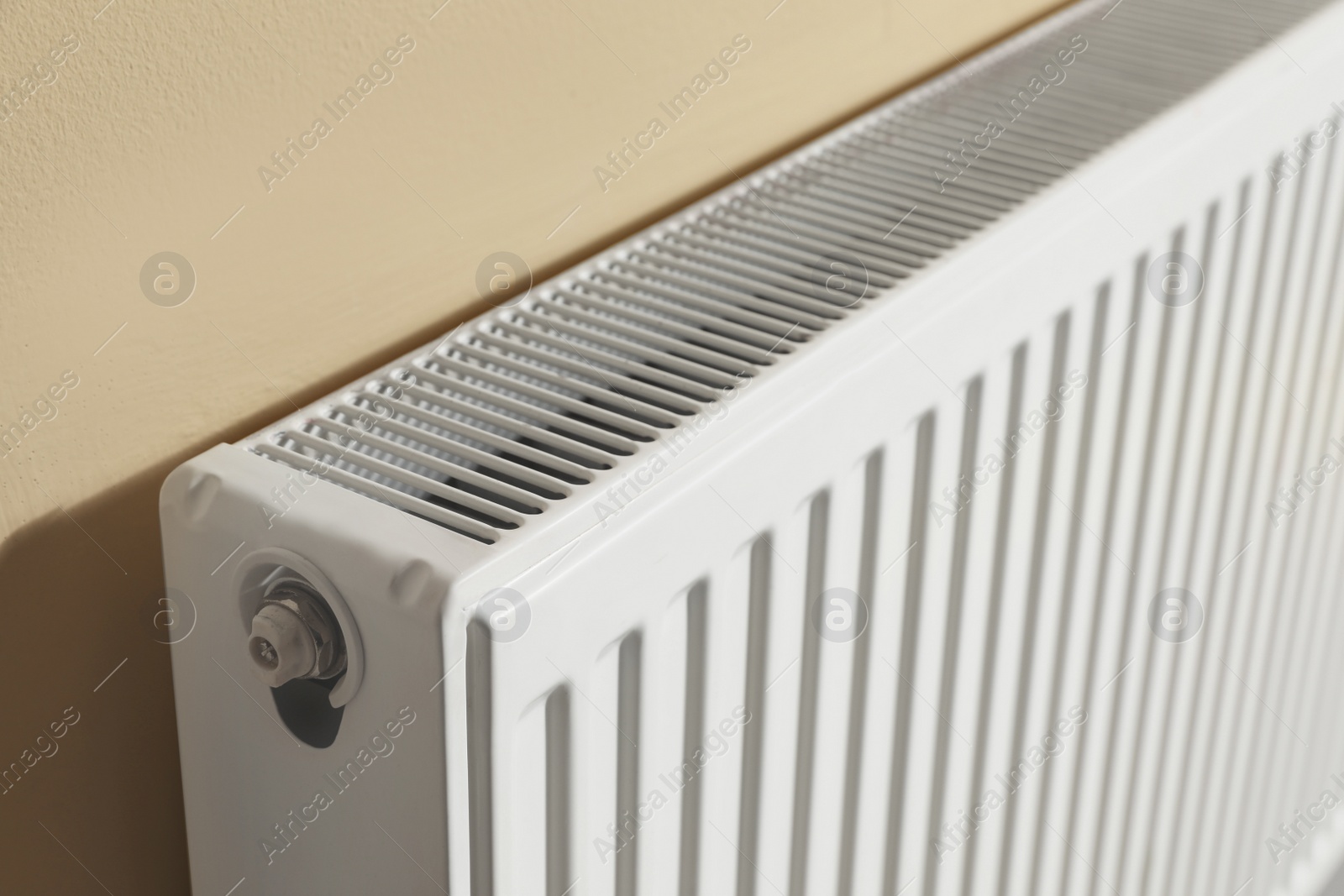 Photo of Modern radiator on beige wall, closeup. Central heating system