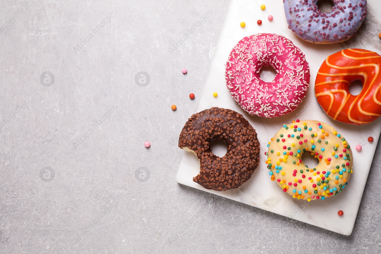 Photo of Yummy donuts with sprinkles on light grey table, top view. Space for text