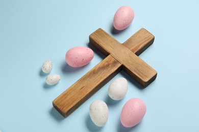 Wooden cross and painted Easter eggs on light blue background