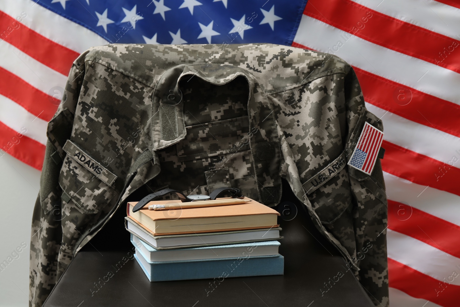 Photo of Books, watch and soldier uniform on chair near flag of United States. Military education