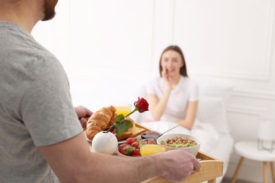 Photo of Romantic breakfast. Husband bringing tray with tasty food to his wife in bedroom, closeup. Space for text