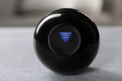 Photo of Magic eight ball with prediction Consult Me Later on light gray table, closeup
