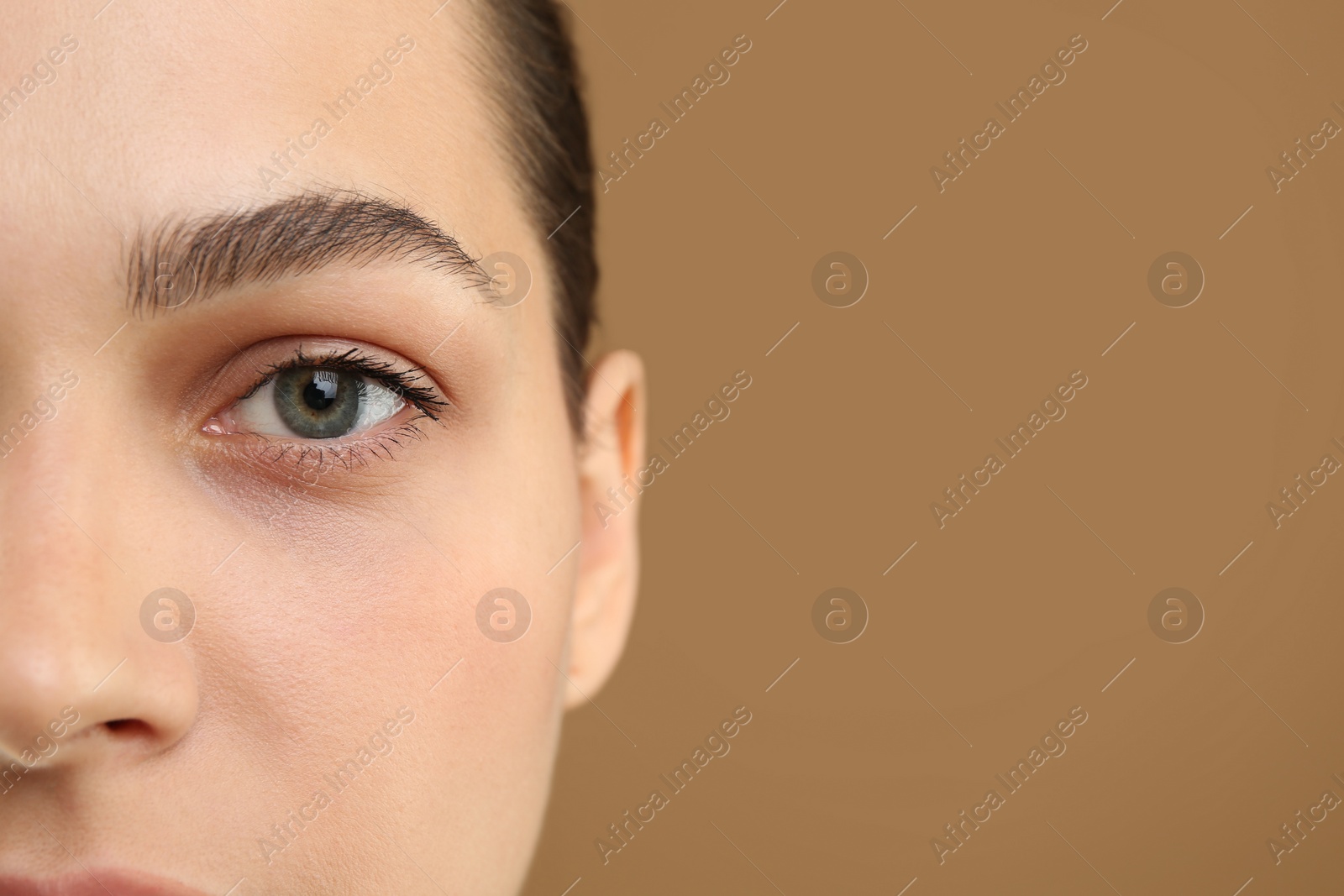 Photo of Young woman with perfect eyebrows on brown background, closeup. Space for text