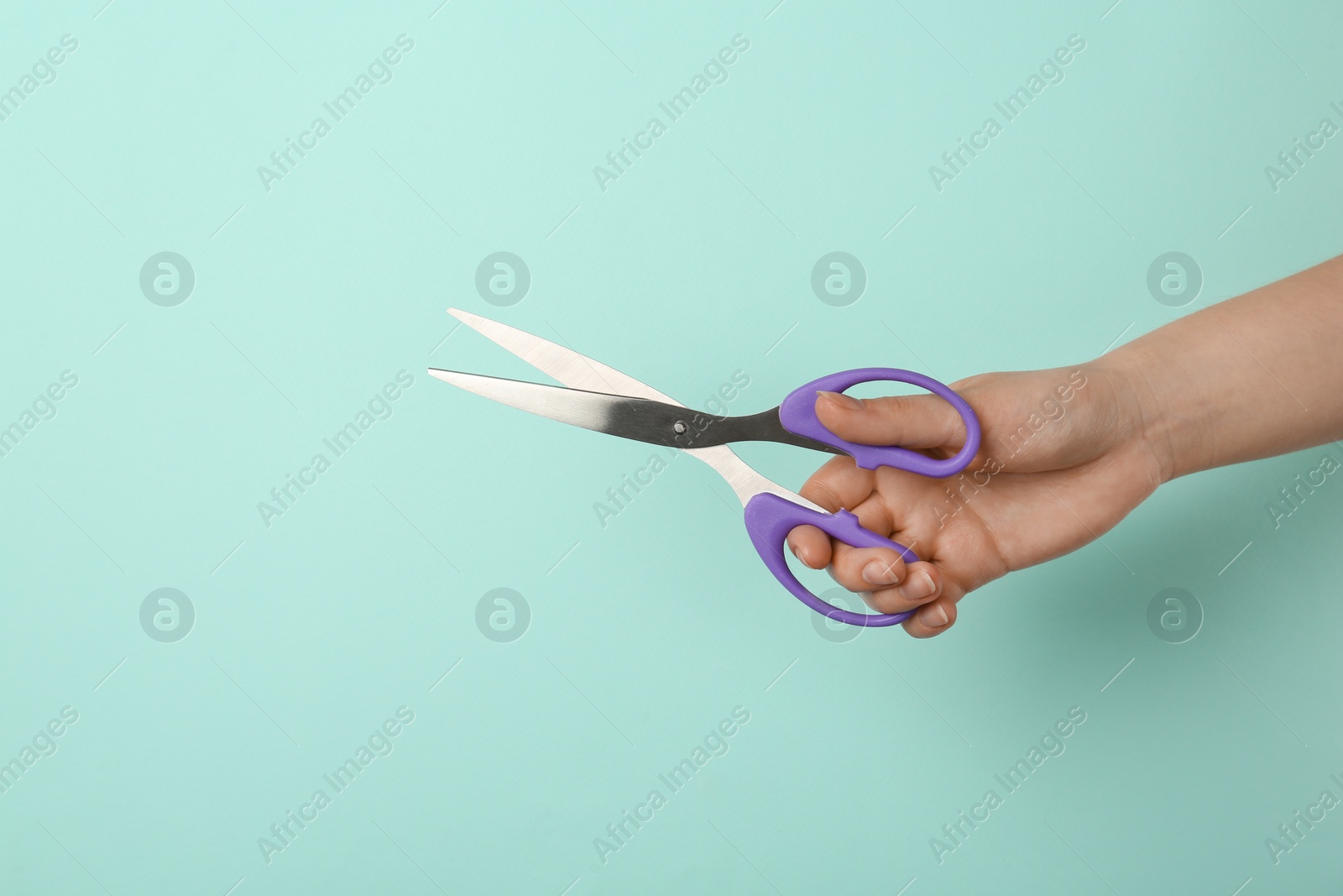 Photo of Woman holding office scissors on light blue background, closeup