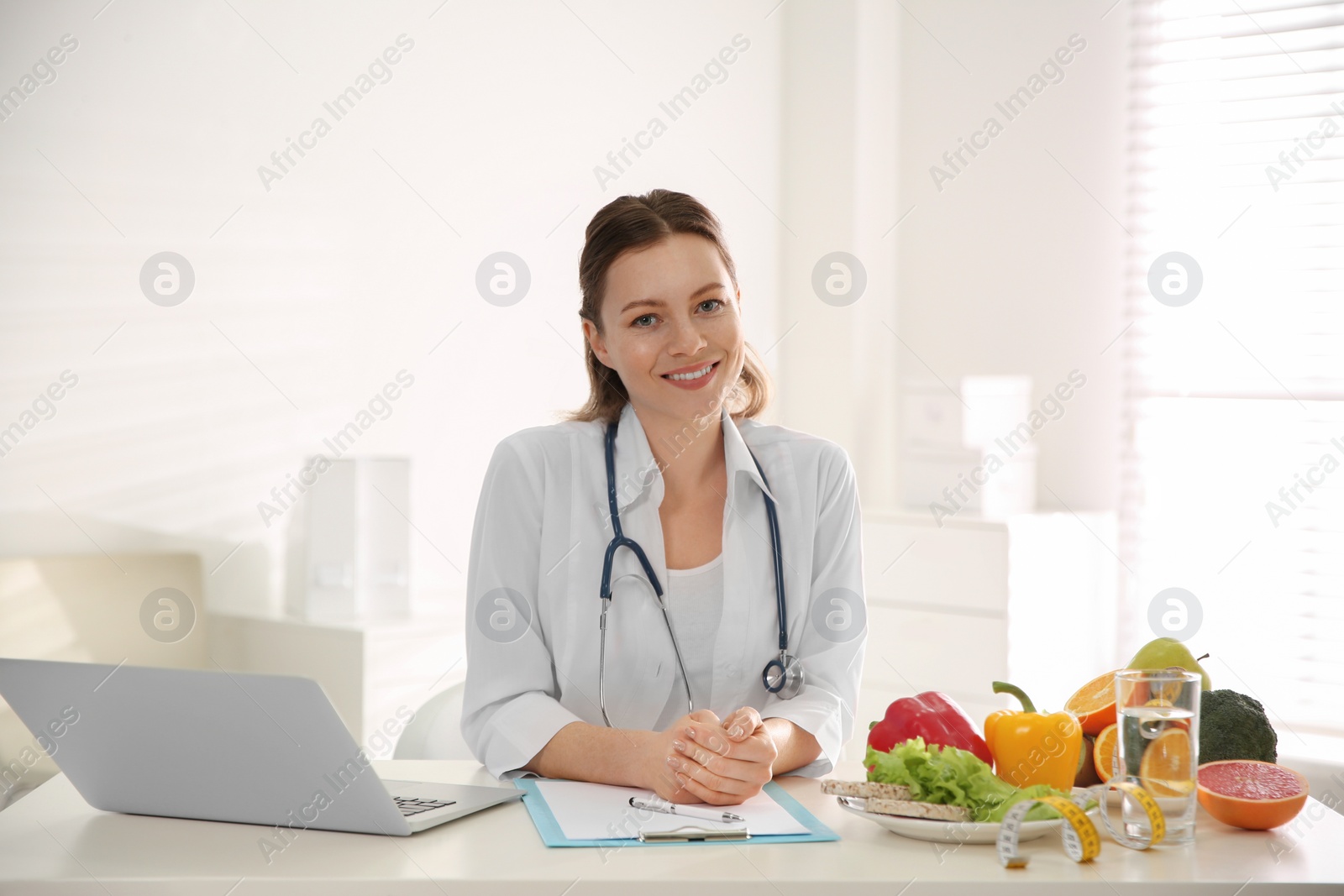 Photo of Nutritionist with clipboard and laptop at desk in office