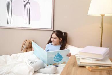 Little girl reading book in bed at home