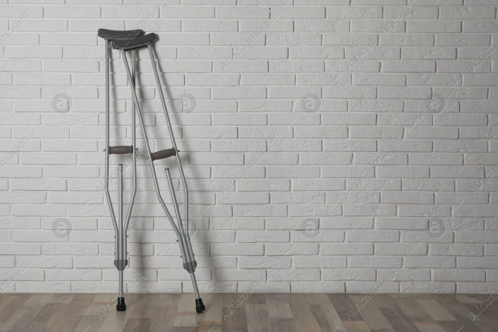 Photo of Pair of axillary crutches near white brick wall. Space for text