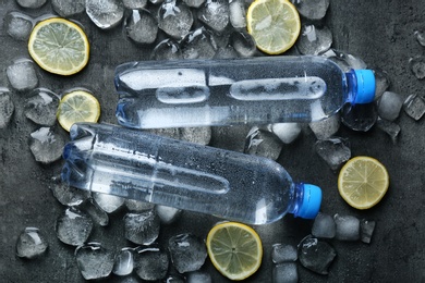Photo of Flat lay composition with bottles of water, lemon slices and ice cubes on dark background