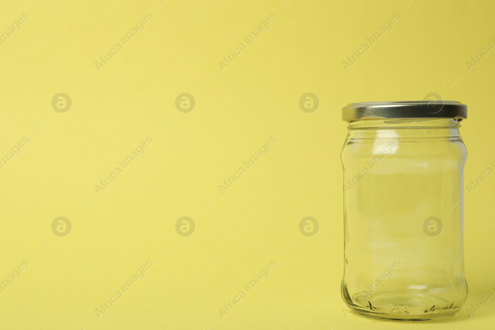 Photo of Closed empty glass jar on light yellow background, space for text