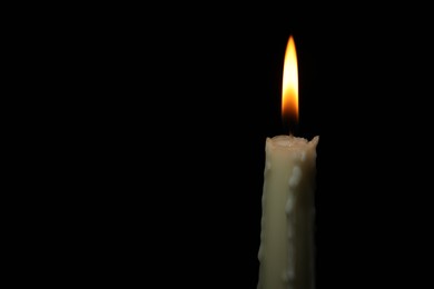 Photo of Burning wax candle on black background, closeup. Space for text