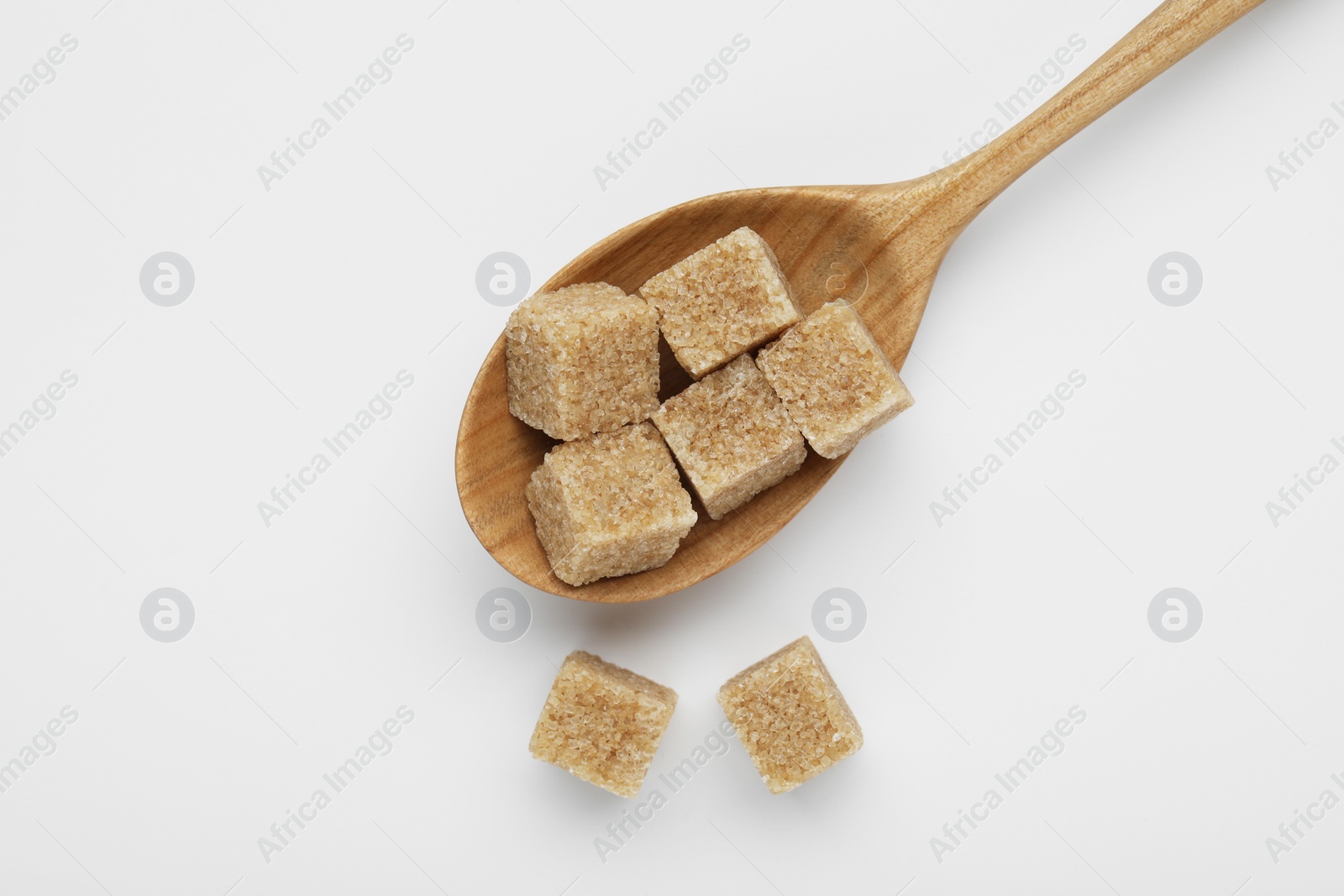 Photo of Brown sugar cubes in wooden spoon on white background, top view