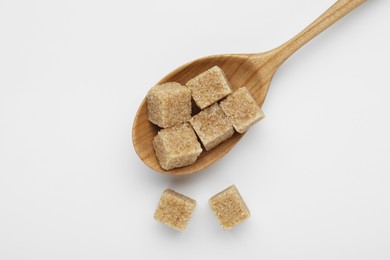 Brown sugar cubes in wooden spoon on white background, top view