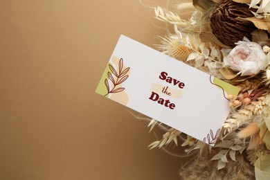 Photo of Beautiful card with Save the Date phrase and dry flowers on beige background, above view. Space for text