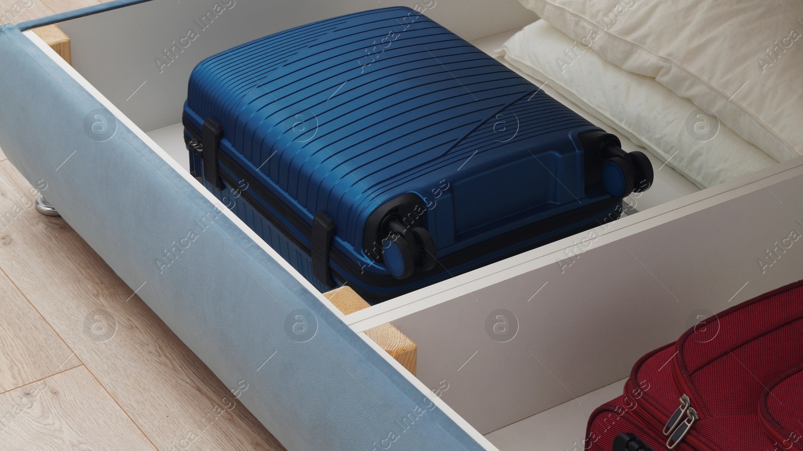 Photo of Storage drawer under bed with blue suitcase and white pillows indoors, closeup