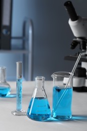 Different laboratory glassware with light blue liquid on table