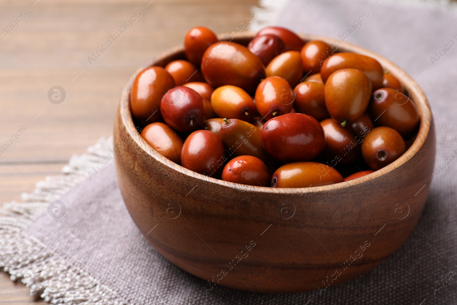 Photo of Fresh Ziziphus jujuba fruits in wooden bowl on table, closeup