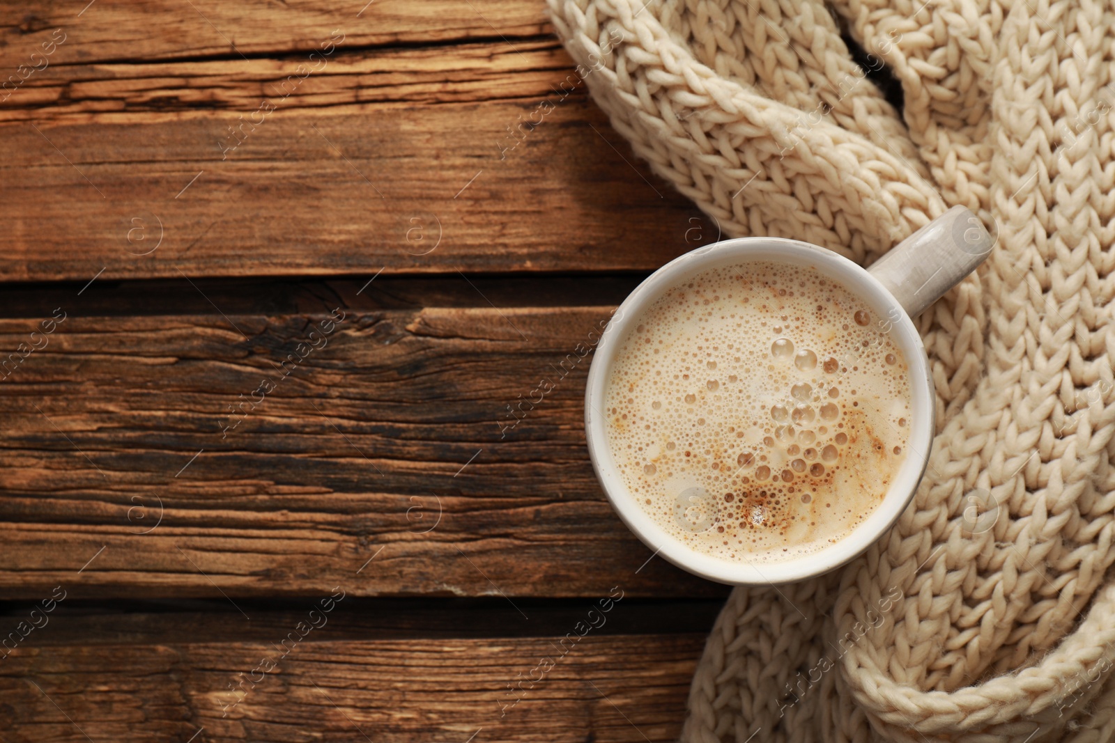 Photo of Top view of coffee and knitted scarf on wooden table, space for text. Cozy winter