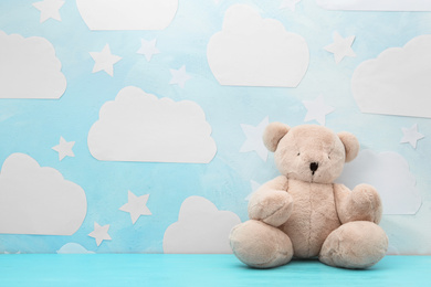 Photo of Teddy bear on wooden table near wall with blue sky, space for text. Baby room interior