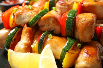 Delicious chicken shish kebabs with vegetables and lemon on plate, closeup