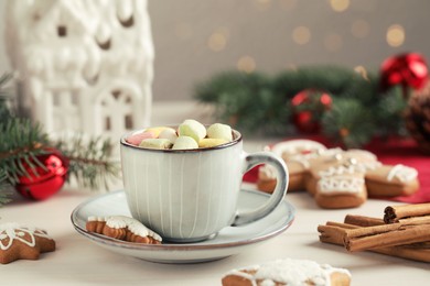 Photo of Delicious hot chocolate with marshmallows and gingerbread cookies on white wooden table against blurred festive lights