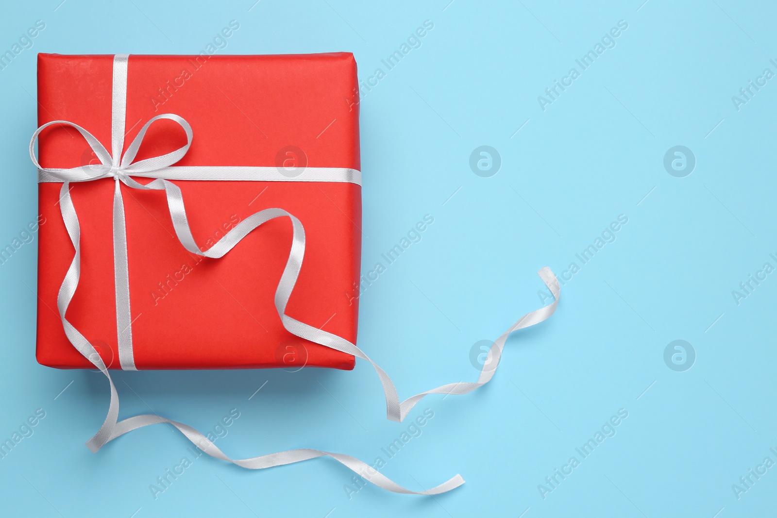 Photo of Beautiful gift box with white bow on light blue background, top view. Space for text