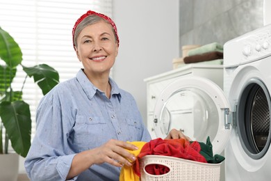 Photo of Happy housewife with laundry basket near washing machine at home