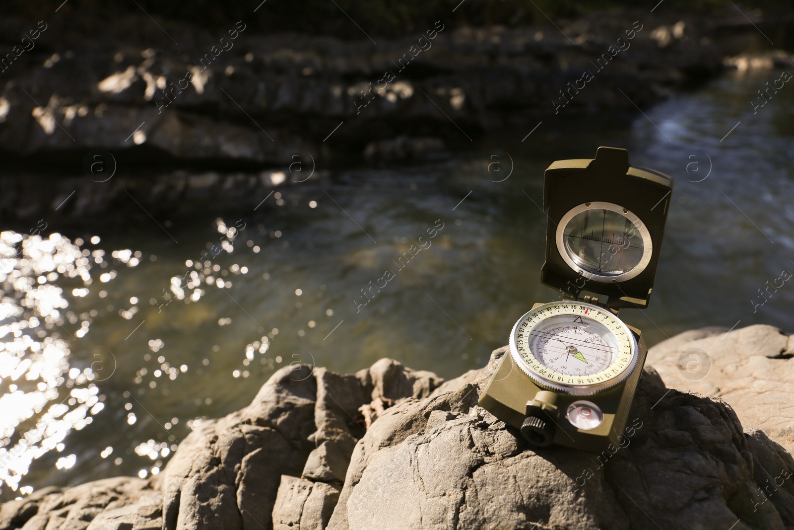 Photo of Compass on rock near river. Space for text