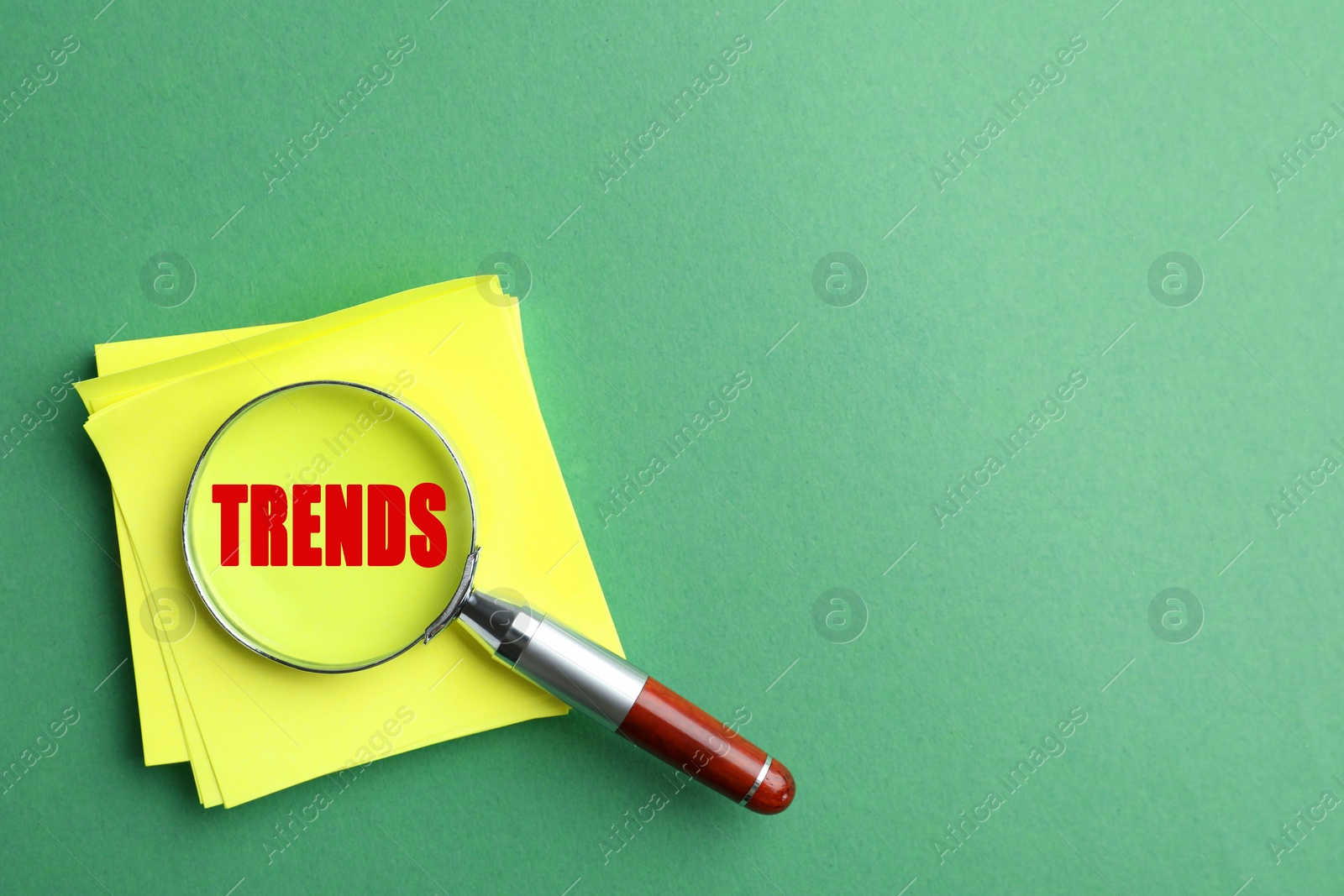 Image of Searching new and popular trends. Magnifying glass with word on paper sheets on green background, top view. Space for text