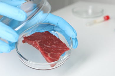 Photo of Scientist holding Petri dish with piece of raw cultured meat in laboratory, closeup