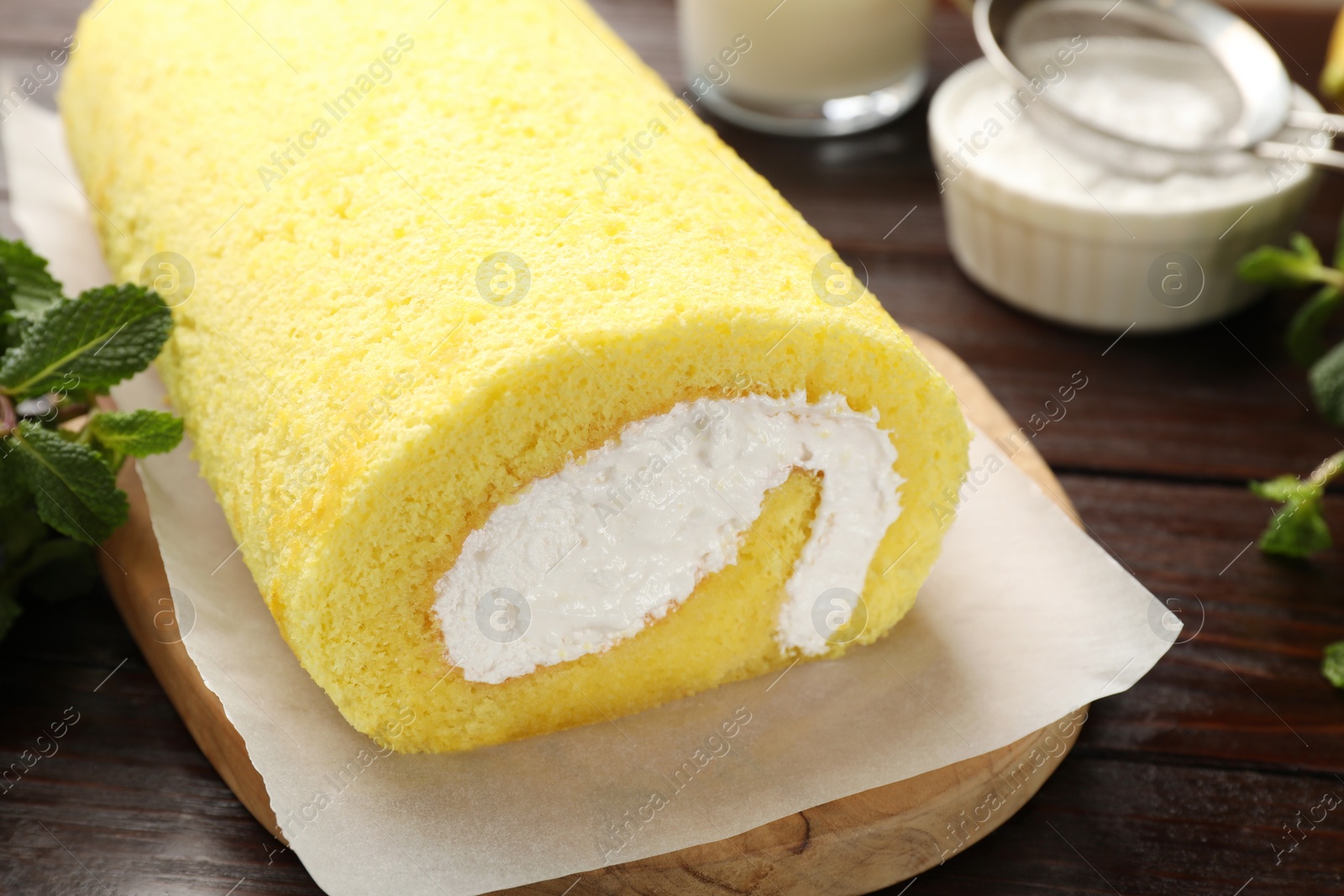 Photo of Delicious cake roll and mint on wooden table, closeup