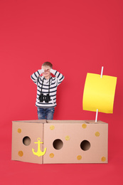 Photo of Little child playing with ship made of cardboard box on red background