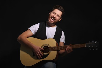 Handsome man with acoustic guitar singing while woman holding microphone on dark background, closeup