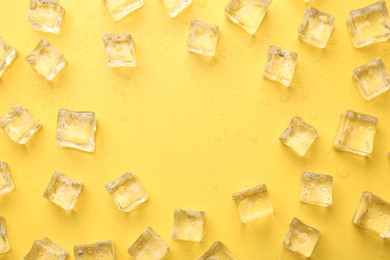 Photo of Crystal clear ice cubes on yellow background, flat lay. Space for text