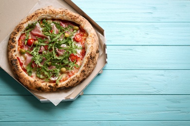 Photo of Tasty pizza with meat and arugula in cardboard box on light blue wooden table, top view. Space for text