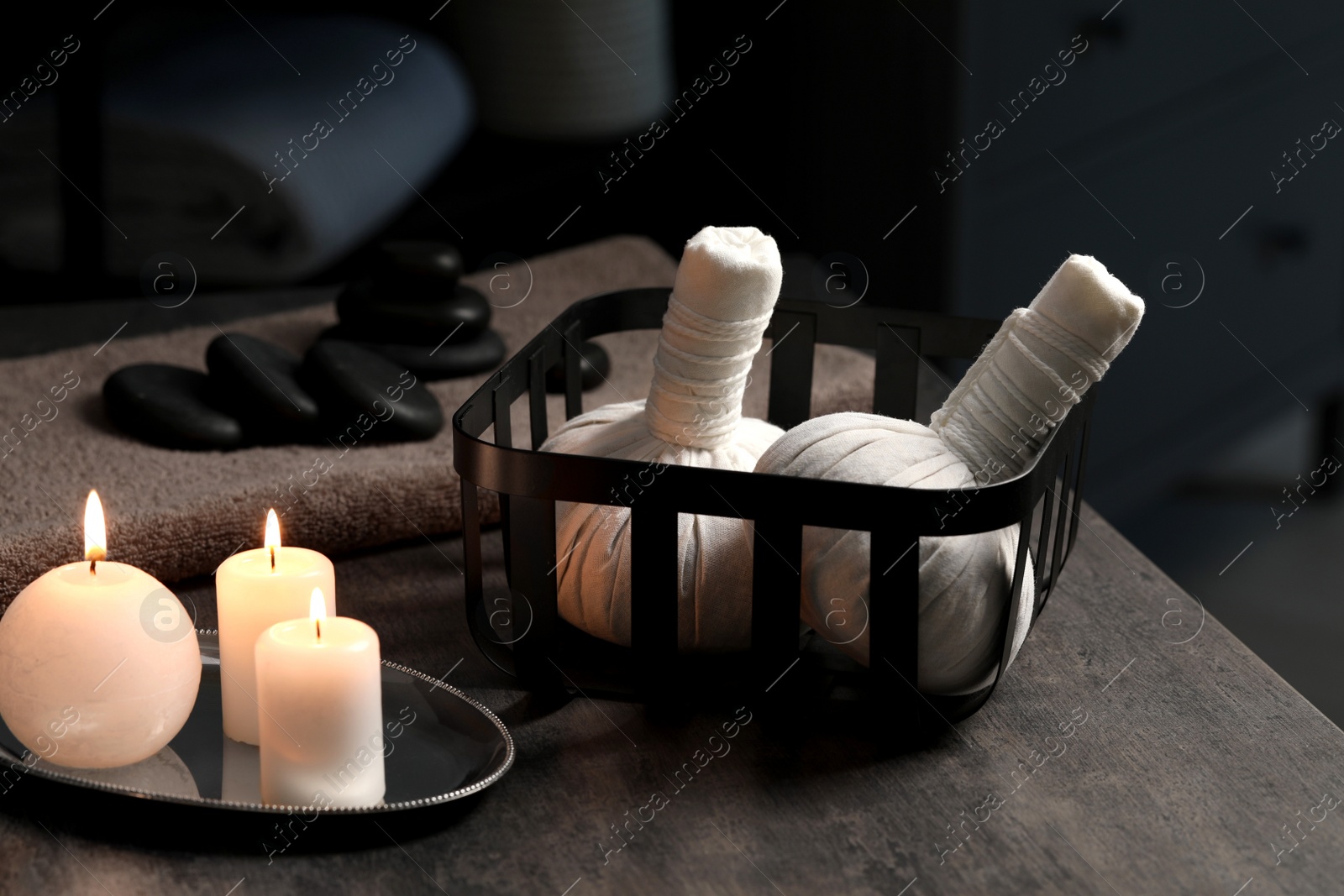 Photo of Herbal massage bags, burning candles and stones on grey table. Spa products