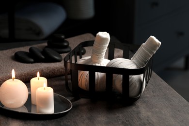 Photo of Herbal massage bags, burning candles and stones on grey table. Spa products