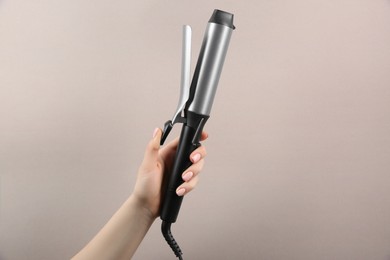 Photo of Hair styling appliance. Woman holding curling iron on light grey background, closeup