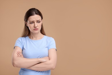 Portrait of sad woman with crossed arms on beige background, space for text