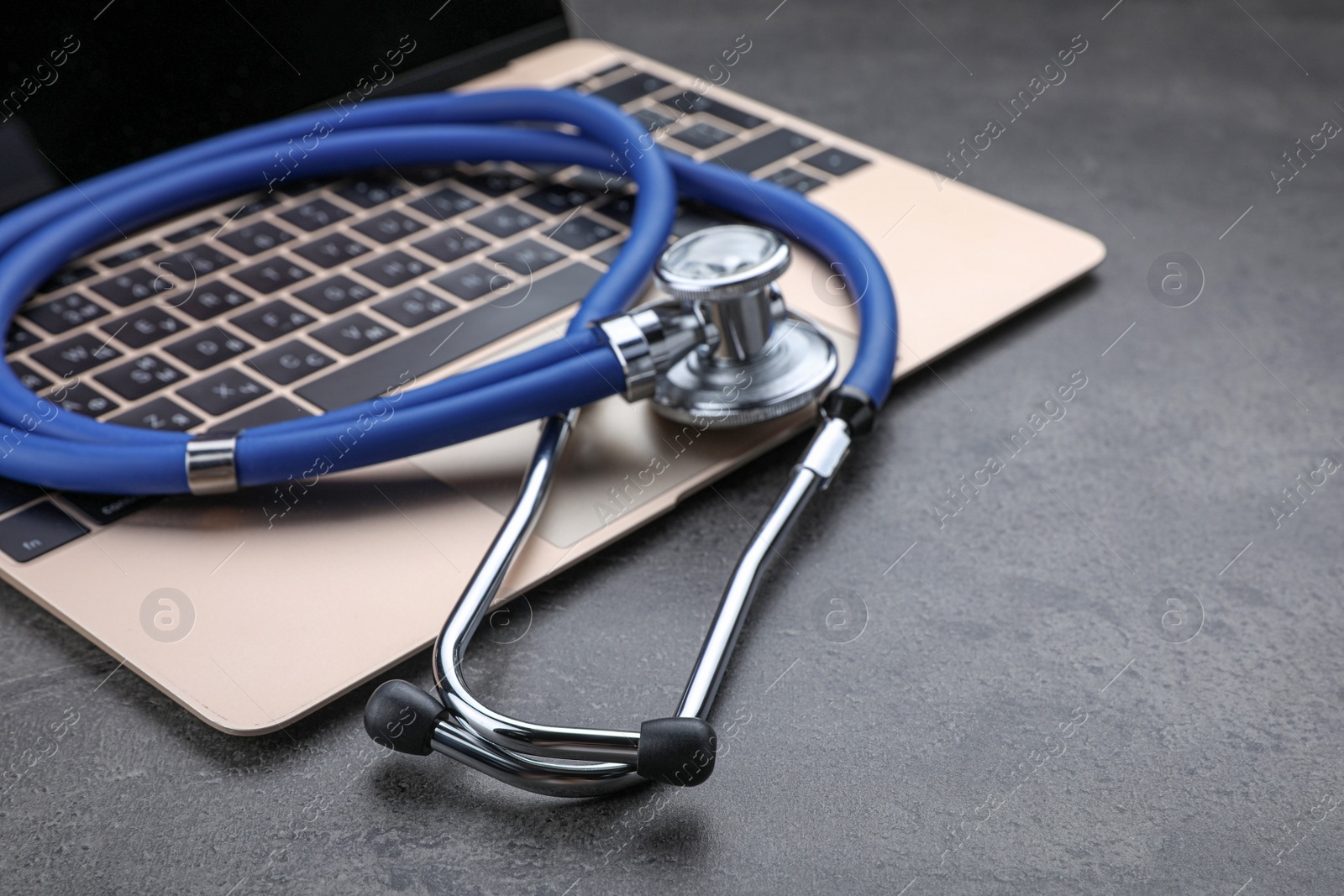 Photo of Laptop with stethoscope on grey table, closeup. Space for text