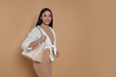 Young woman with stylish bag on beige background, space for text