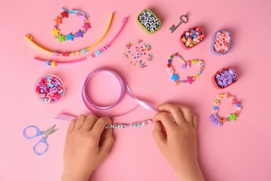 Photo of Child making beaded jewelry and different supplies on pink background, top view. Handmade accessories